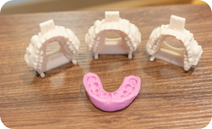 Pink mold of a row of teeth next to three tooth colored devices shaped like a row of teeth