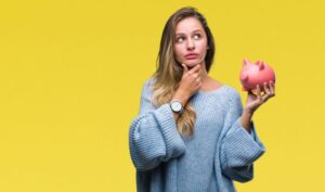 Woman touching her chin while holding a piggy bank